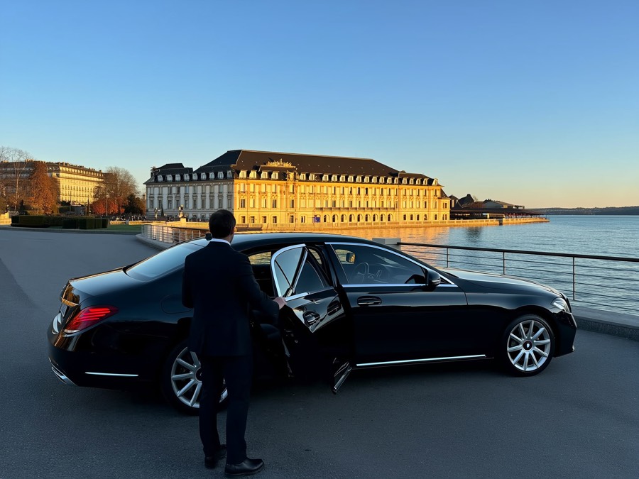 Berline noire haut de gamme, chauffeur ouvrant la portière devant un hôtel au bord du lac